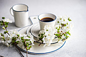 Elegant gedeckter Tisch mit weißen Kirschblüten und einer Tasse Kaffee vor einem ruhigen Hintergrund