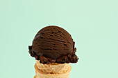 Scoop of chocolate ice cream in a waffle cone in green background