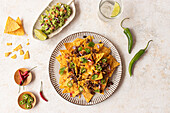 Top view of a delectable plate of nachos generously topped with cheese, minced meat, and fresh vegetables, alongside a serving of guacamole and a refreshing lime drink.