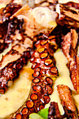 Close-up image of grilled octopus tentacles served with a creamy sauce and fresh herbs, showcasing vibrant colors and textures.