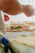 An anonymous chef adds toppings to a pizza, illustrating the culinary process in a pizzeria, with a focus on freshness and skill