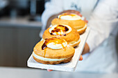 High angle of anonymous crop baker standing with sweet vegan Berliners with sugar crust on board in bakehouse