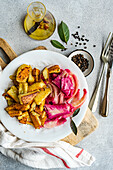 Vibrant dish of spicy fermented cabbage with beetroot paired with golden roasted potatoes, garnished with black pepper and bay leaves.