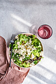 Ein nahrhafter Kräutersalat mit Kopfsalat, grünen Zwiebeln, Petersilie, Estragon, fermentierten Kapern und zerbröckeltem blauem Brie-Käse, beträufelt mit Olivenöl und begleitet von einem Glas Wasser