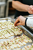 Anonymous chef meticulously adds final toppings to an array of canapes on a stainless steel tray, showcasing the precision of culinary art