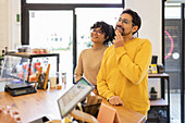 A happy and stylish young multiethnic couple is seen contemplating a purchase in a cozy and modern boutique.