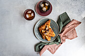 Top view of a refreshing glass of iced tea beside a slice of homemade cherry pie, served on a ceramic plate. Both items are placed on a gray textured surface, accompanied by a green linen napkin.