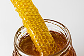 Closeup of piece of honeycomb on top of glass jar full of fresh natural golden honey with white background