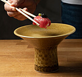 A chef grips a piece of tuna nigiri topped with caviar using chopsticks, hovering above a textured ceramic bowl