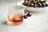 A stylish textured glass holds rich cherry liqueur, accompanied by luscious fresh cherries on a serene background