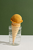 Scoop of dulce de leche ice cream in waffle cone in green background