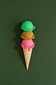 Triple-layered ice cream cone with colorful scoops in green background