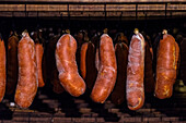 Image showcases several rows of sobrasada sausages, a type of cured meat from the Balearic Islands, aging in a smokehouse setting.