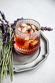 An elegant presentation of a cognac cocktail, served in a crystal cut glass with ice, garnished with a fresh lavender sprig, placed on a vintage silver tray