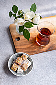 Plate of assorted Turkish delights paired with black tea and a vase of white roses on a wooden board