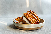 Fresh, homemade waffles with a delicious vanilla marshmallow sandwiched between, presented in a ceramic bowl