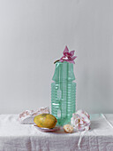 A minimalist still life setup featuring a green plastic with a pink orchid, accompanied by a fruit and some decorative stones on a textured linen cloth Soft, natural light enhances the tranquil mood