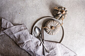 A sophisticated autumnal flat lay featuring ceramic pumpkins, a linen napkin, and cutlery on a textured gray background