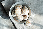 A bowl of traditional cookies dusted with powdered sugar, served on a textured tablecloth