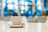 An inviting coffee cup sits on a white table with a blurred cafe background, creating a cozy and relaxing atmosphere