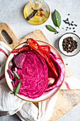 A bowl of colorful fermented cabbage mixed with slices of beetroot, spicy red peppers, and whole garlic cloves, capturing a contrast of textures and flavors.