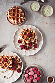 Freshly baked waffles topped with whipped cream and raspberries, accompanied by green smoothies, perfect for a delicious breakfast or brunch setting