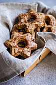 Top view of homemade gingerbread star-shaped cookies dusted with cinnamon, resting on a grey linen cloth in a wooden box, displaying holiday vibes.