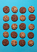 A flat lay photograph of twelve cookies arranged on a vibrant blue background, featuring a mix of chocolate chip and double chocolate cookies. The contrast between the two types of cookies makes a visual impact