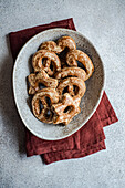 Draufsicht auf selbstgebackene Lebkuchen in Sternform, bestäubt mit Zuckergewürz, kunstvoll präsentiert in einer gesprenkelten Keramikschale auf einer strukturierten grauen Oberfläche mit einem weinroten Tuch.