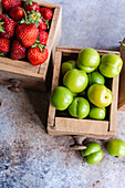 Organic ripe strawberries, sweet cherries, and green plums arranged in vintage wooden boxes on a textured surface, showcasing nature's colorful bounty