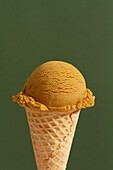 Scoop of dulce de leche ice cream in waffle cone in green background