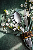 Elegant spoon, fork, and knife tied together, set on a green napkin with cherry blossoms