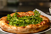 Dieses Bild zeigt eine frisch gebackene Pizza, die mit Rucola, Oliven und Kirschtomaten belegt ist. Die goldene Kruste ist perfekt gegart und bietet einen verlockenden Anblick für Liebhaber von Lebensmitteln und kulinarischen Themen