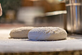 This image captures the early stage of pizza preparation, showing raw dough sprinkled with flour, ready for shaping and baking