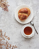 Draufsicht auf ein herbstliches Teeservice mit einer Tasse heißem Tee und einem frisch gebackenen Sesambrot auf einer strukturierten Oberfläche, begleitet von Trockenblumen