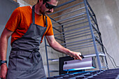 A focused urban farmer adjusts LED grow lights over trays of microgreens in an indoor farming setup, showcasing modern sustainable agriculture techniques