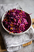 A healthy lunch set featuring a vibrant raw red cabbage and carrot salad paired with fluffy boiled bulgur, presented in a white bowl on a gray linen napkin