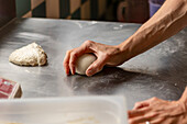 A close-up image capturing the hands of a chef kneading pizza dough on a metallic counter, showcasing the early stages of pizza preparation