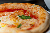 This close-up image captures a freshly baked pizza with a golden crust, melting cheese, bright tomato sauce, and a hint of basil The focus is on the textures and vibrant colors of the pizza