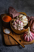 Ein warmes, einladendes Foto mit frischem Knoblauch und lebendigen Gewürzen. Eine Holzschüssel mit Knoblauchzehen und eine weitere mit feinen orangefarbenen Gewürzen, alles auf einem rustikalen Holzbrett angeordnet