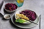 A well-balanced diet meal featuring red cabbage and carrot salad alongside boiled bulgur, served on a stylish grey plate with green onions, perfect for a nutritious lunch