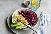 A nutritious meal featuring boiled bulgur paired with a vibrant red cabbage and carrot salad on a light gray plate, complemented by green onions and a refreshing drink