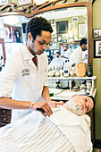 Professioneller Friseur und Haarschneider rasiert seinen Kunden im Schorem Barber Shop am Nieuwe Binnenweg, Rotterdam, Niederlande.