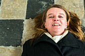 Breda, Netherlands. Mid adult caucasian woman lying down on a mediaval church floor while smiling with joy.