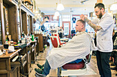 Professioneel barbier verzorgt het haar van een van zijn mannelijke klanten in de barbershop.