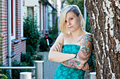 Porträt Junge Frau mit Tatoos in lehnte gegen Baum in Residential Garden. Tilburg, Niederlande.