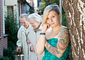 Portrait Young Woman with Tatoos in leaning aginst Tree in Residential Garden. Tilburg, Netherlands.