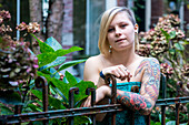 Portrait Junge Frau mit Tatoos im Wohngarten. Tilburg, Niederlande.