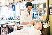 Professioneller Friseur und Haarschneider rasiert seinen Kunden im Schorem Barber Shop am Nieuwe Binnenweg, Rotterdam, Niederlande.