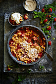 Homemade strawberry crumble, served with whipped cream on a gray metal surface